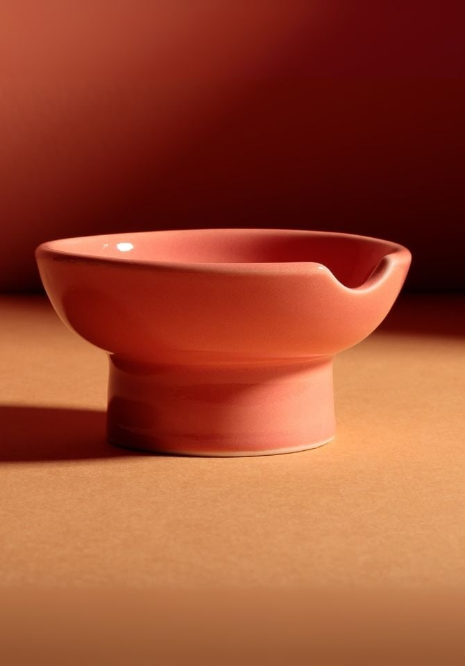 Orange ceramic barrow bowl ashtray on a matching coral backdrop, showing its smooth curved rim and pedestal base
