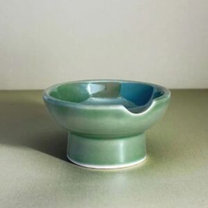 Our ceramic ashtray, in iridescent green, elevates any decor with its midcentury footed design
